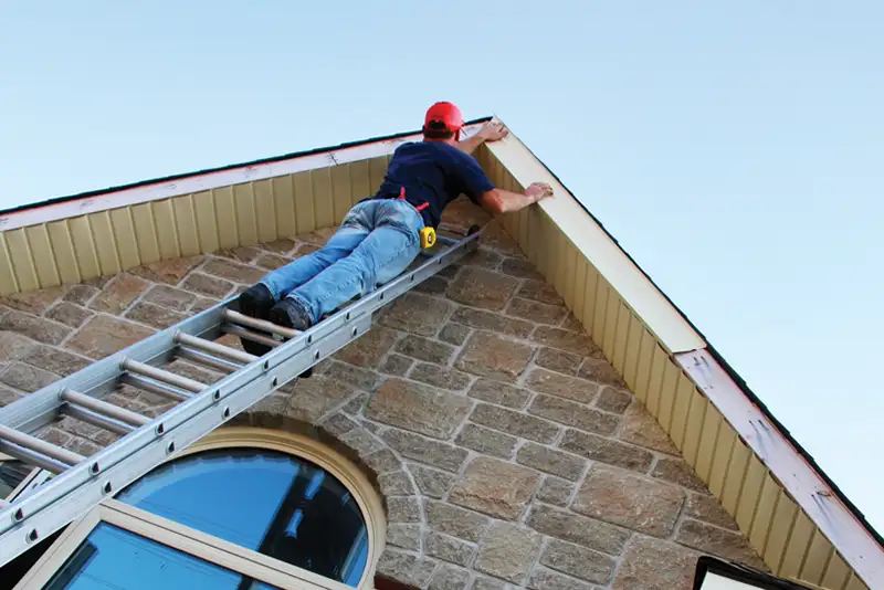 Professional on a ladder is inspecting/repairing soffit and fascia of residential home - Clinton County, IL