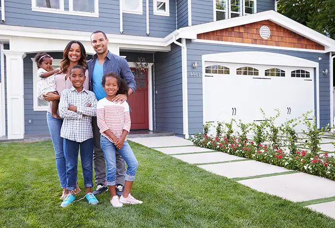 Happy African American family, with mom dad and three kids posing in front of new house with beautiful siding and guttering - Clinton County, IL